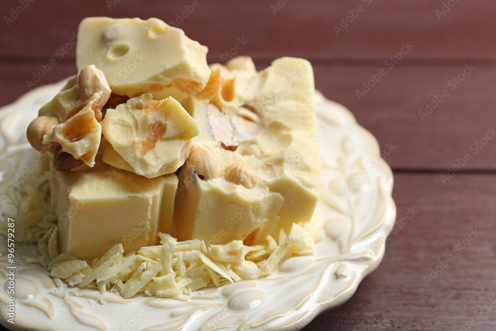 White chocolate pieces with nuts on plate, on color wooden background White chocolate pieces with nuts on plate, on color wooden background