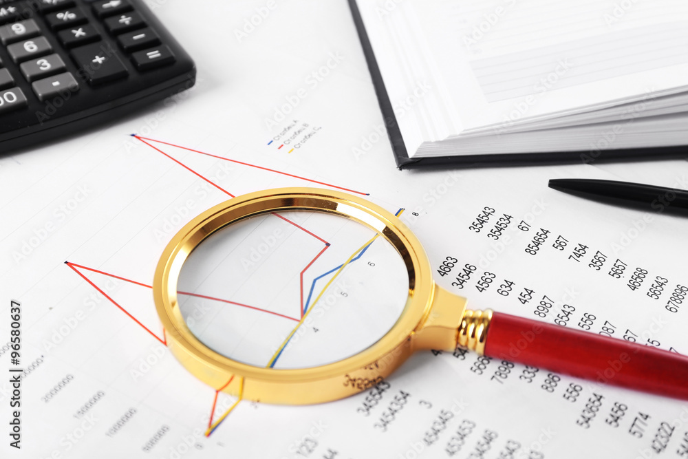 A magnifying glass on financial documents background, close-up A magnifying glass on financial documents background, close-up