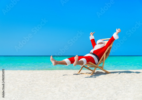 Christmas Santa Claus resting on sunlounger at ocean sandy tropical beach