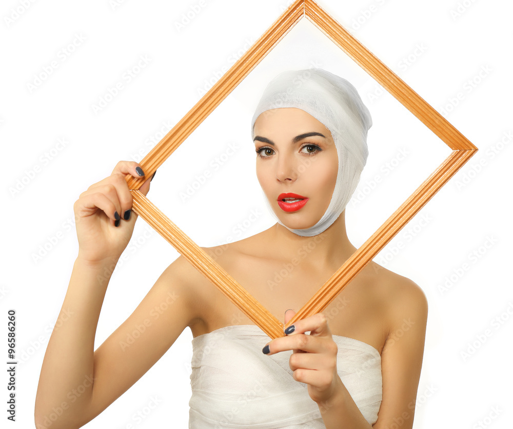 Young beautiful woman with a gauze bandage on her head and chest, holding a frame, isolated on white