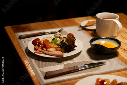 Served dinner with ham, greens, cup and desert on a table with soft warm light