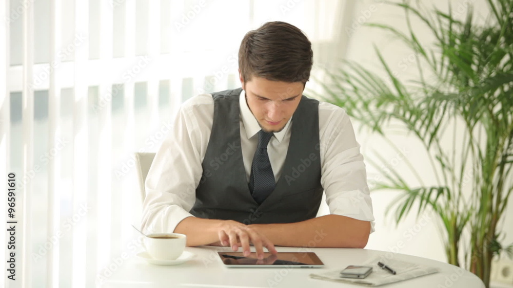 Attractive man sitting at table and using touchpad Attractive man sitting at table and using touchpad