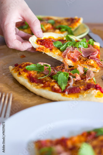 Female hand grabs for a slice of italian style pizza with arugula and prosciutto
