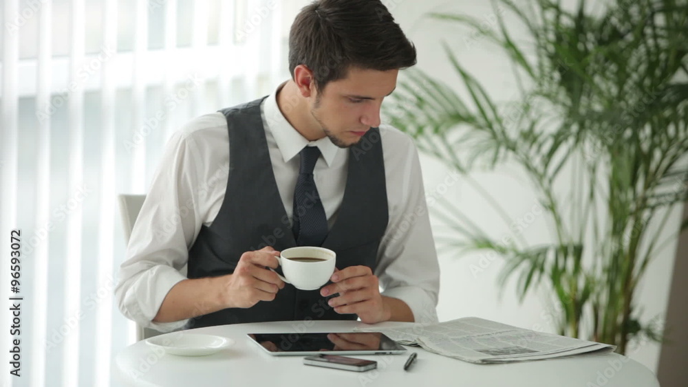 Charming man sitting at table reading newspaper and drinking coffee Charming man sitting at table reading newspaper and drinking coffee
