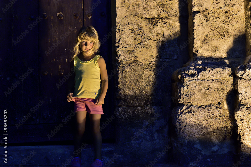 Night shot of little girl leaning against old building at street