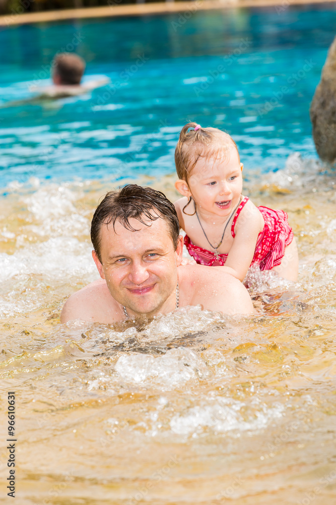 Active father teaching his toddler daughter to swim in pool on tropical resort. Summer vacations and sport concept Active father teaching his toddler daughter to swim in pool on tropical resort. Summer vacations and sport concept