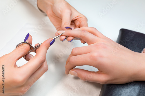 Manicurist cut clients cuticle with nail scissors
