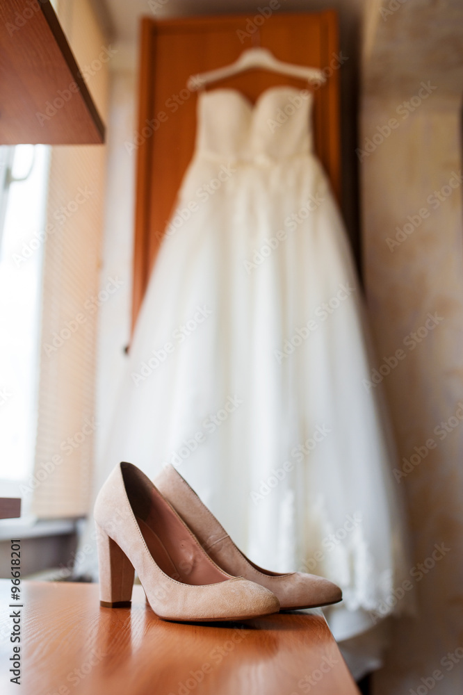 Beautiful white bridal shoes and dress at luxurious bedroom