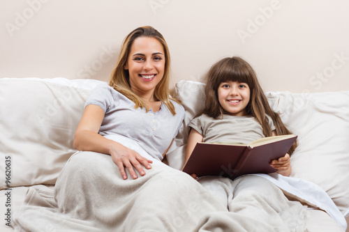Mother and daughter reading together book in bed 