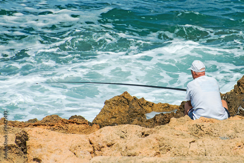 Man fishing on rocks by the sea.