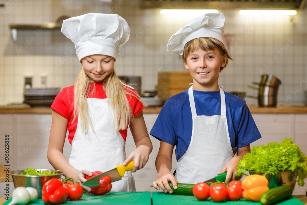 Funny happy chef boy and girl cooking at restaurant kitchen. concept of vegetarianism Funny happy chef boy and girl cooking at restaurant kitchen. concept of vegetarianism