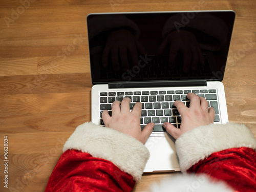 Santa working at desk and typing on a laptop, Christmas gifts an