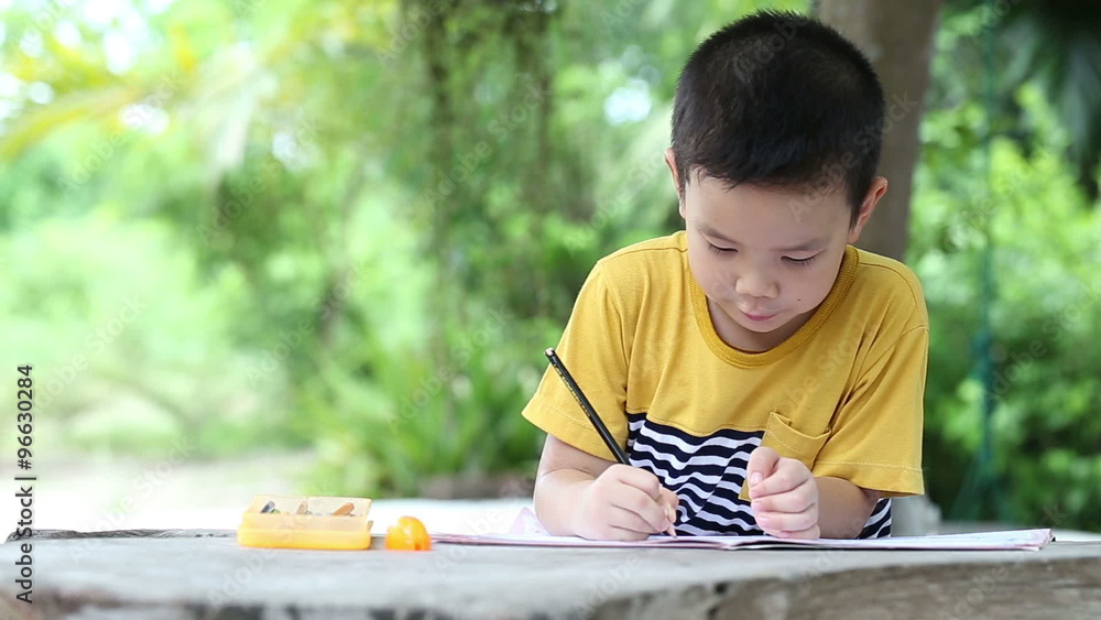 Little asian boy use pencil writing on notebook for writing book with smiling face on wooden table in the park Little asian boy use pencil writing on notebook for writing book with smiling face on wooden table in the park