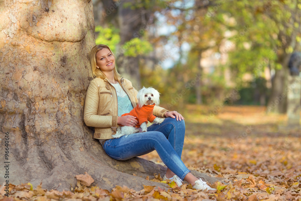 Young woman enjoying nice autumn day in a park with her cute little Maltese dog Young woman enjoying nice autumn day in a park with her cute little Maltese dog