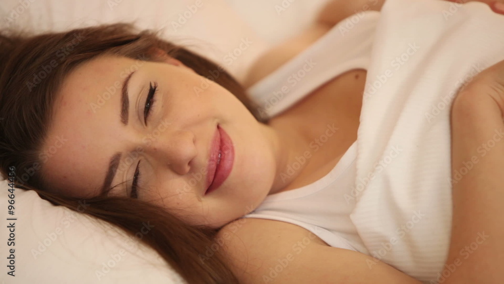 Attractive girl sleeping in bed waking and smiling at camera then falling asleep again. Panning camera Attractive girl sleeping in bed waking and smiling at camera then falling asleep again. Panning camera