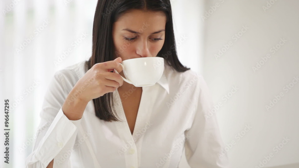 Charming girl sitting at office desk working on laptop drinking tea looking at camera and smiling. Panning camera Charming girl sitting at office desk working on laptop drinking tea looking at camera and smiling. Panning camera