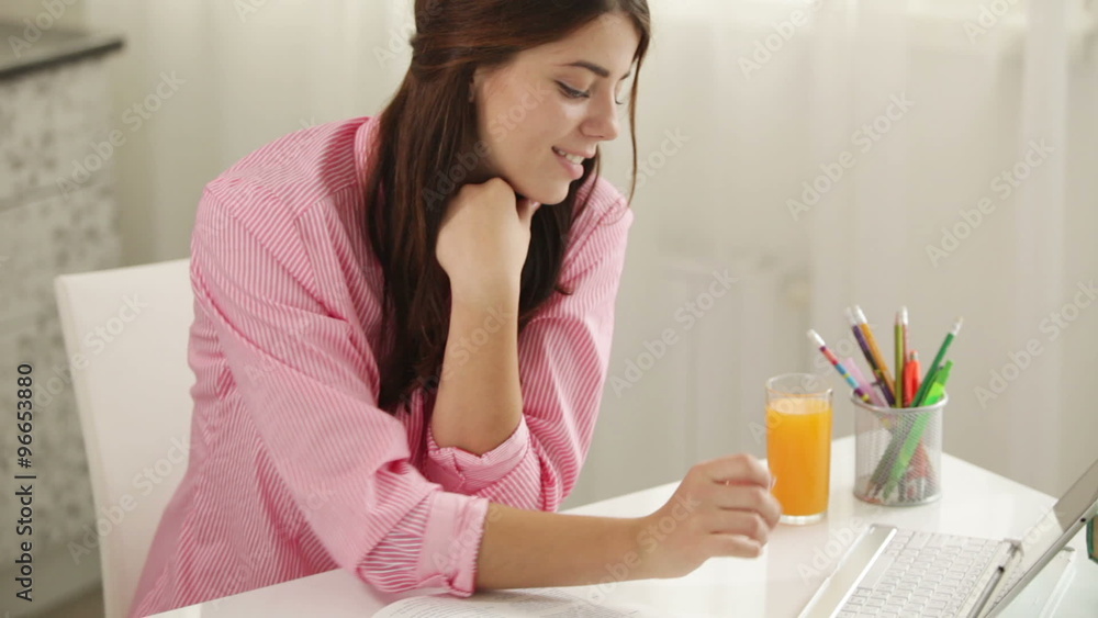 Cheerful student girl sitting at table using laptop looking at camera and smiling. Panning camera Cheerful student girl sitting at table using laptop looking at camera and smiling. Panning camera