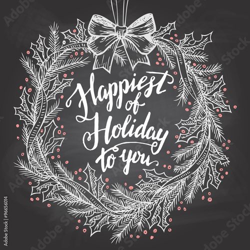 Happiest of holiday to you. Calligraphy quote with Christmas wreath on blackboard with chalk
