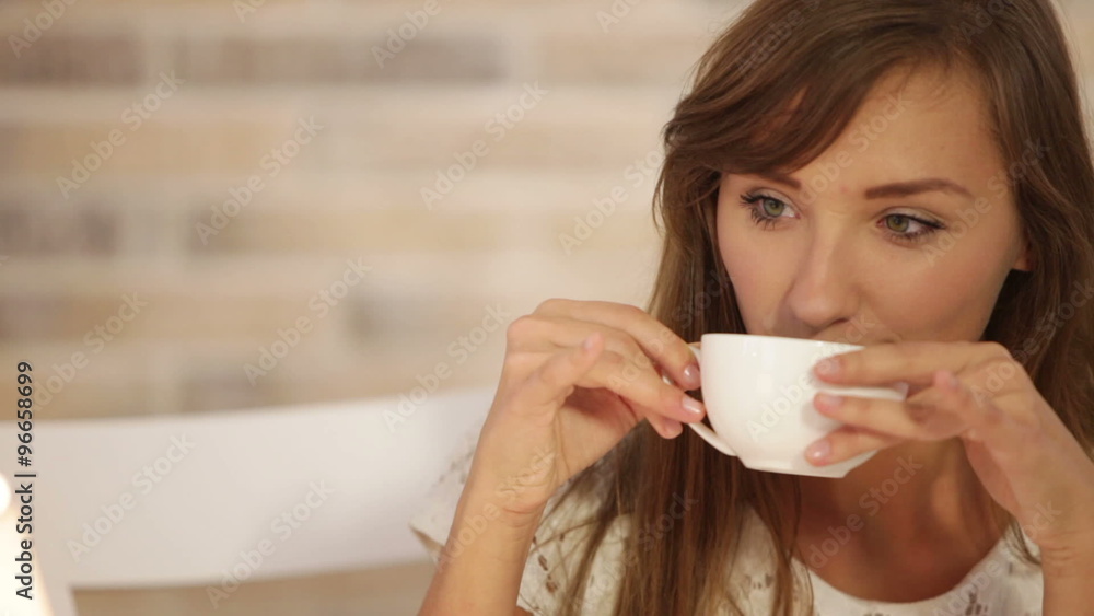 Pretty young woman sitting at cafe drinking tea looking at camera and smiling. Panning camera Pretty young woman sitting at cafe drinking tea looking at camera and smiling. Panning camera
