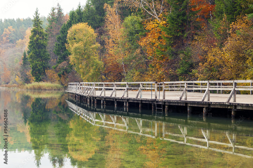 Calm autumn landscape with colorful trees and wooden pier reflected in the lake water