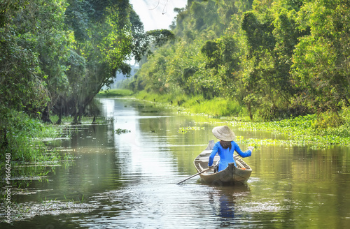 Woman rowing on the river and passed the house homeland with small body, shirt Ba Ba and conical hats typical of Southeast women in a spring afternoon in Dong Thap, Vietnam