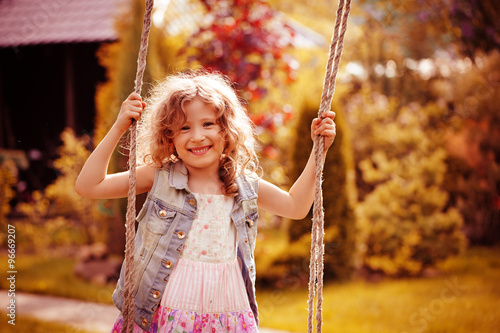 happy child girl relaxing on swing in spring garden, spring vacation outdoor activities