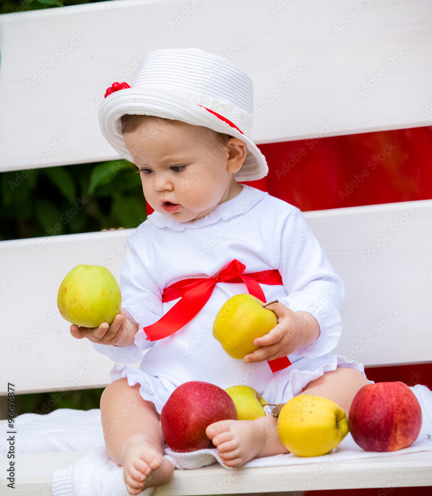 Beautiful baby girl with apples on a bench in a summer garden Beautiful baby girl with apples on a bench in a summer garden