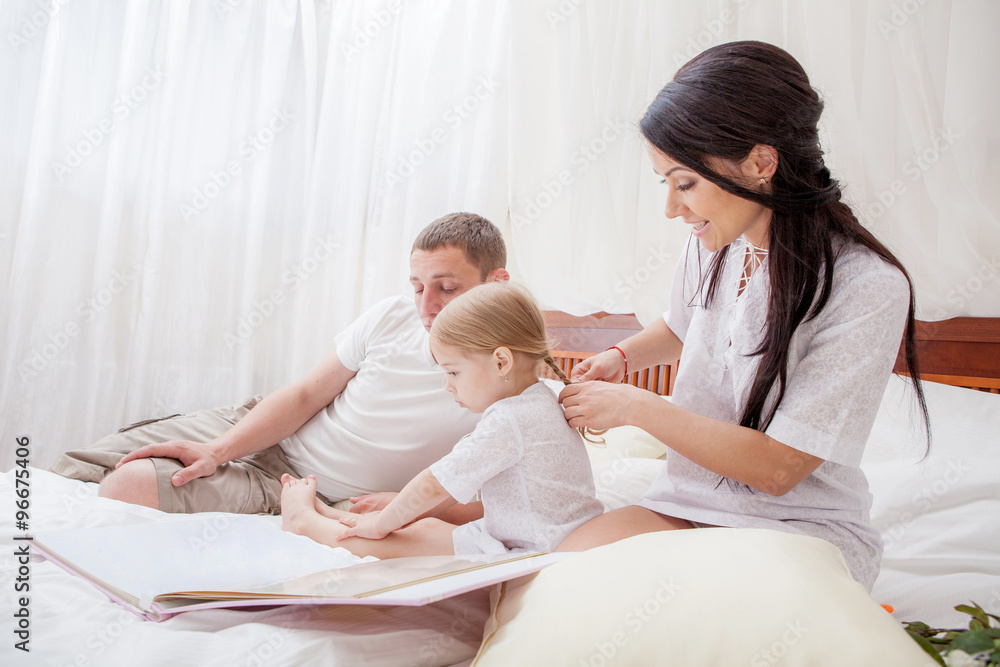 Portrait of a little girl reading with her parents in bed Portrait of a little girl reading with her parents in bed