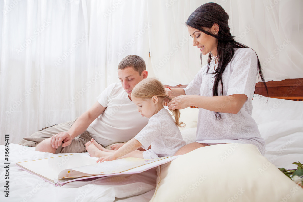 Portrait of a little girl reading with her parents in bed Portrait of a little girl reading with her parents in bed