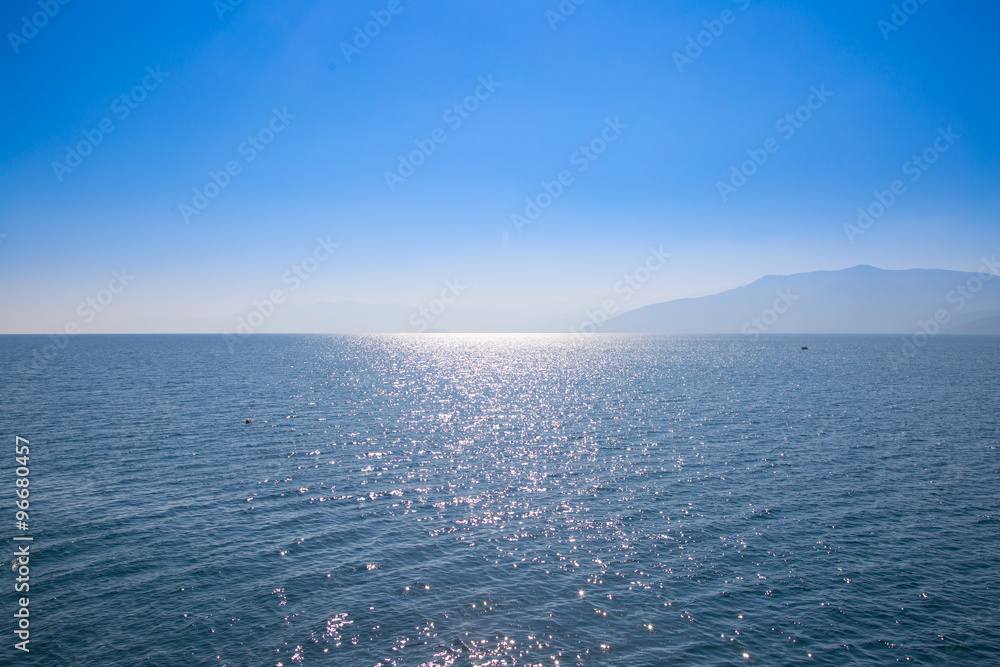 Naklejka premium Seascape with blue sky and waters, with distant land hidden in the mist.