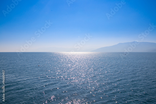 Seascape with blue sky and waters, with distant land hidden in the mist.