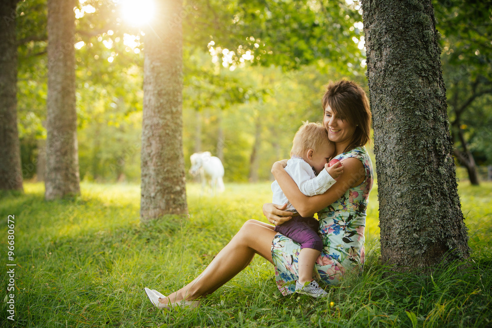 Mom and son sitting in a meadow on a sunny summer day, the boy hiding in his mother's bosom. Mom and son sitting in a meadow on a sunny summer day, the boy hiding in his mother's bosom.