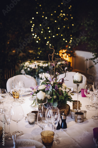 A table laid for a special occasion, with a floral centrepiece and candles, at night. 