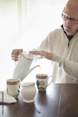 Man sitting at table, pouring coffee into cup photo