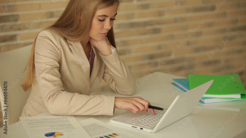 Charming young woman sitting at table using laptop looking at camera and smiling. Panning camera Charming young woman sitting at table using laptop looking at camera and smiling. Panning camera