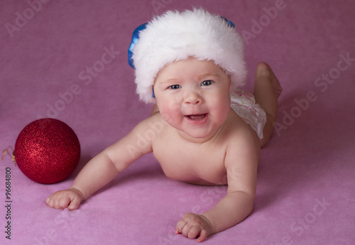 Joyful little baby in Christmas hat and Christmas decoration on a pink background 