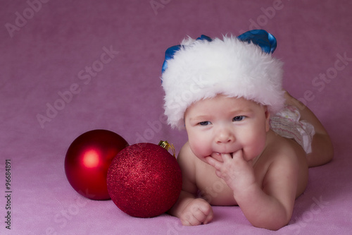 Joyful little baby in Christmas hat and Christmas decoration on a pink background 
