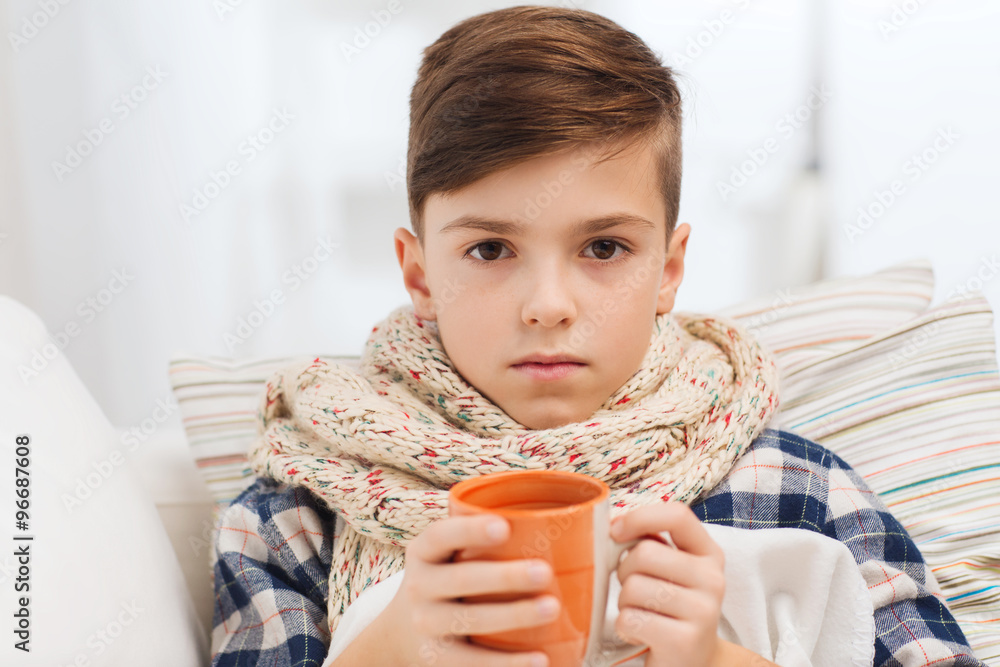ill boy with flu in scarf drinking tea at home ill boy with flu in scarf drinking tea at home