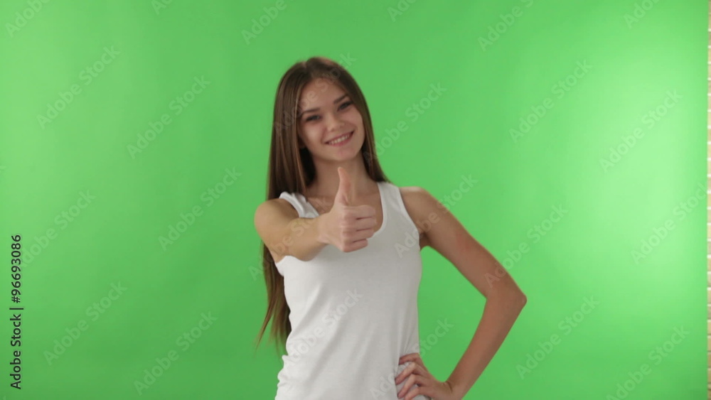 Charming girl standing on green background smiling and showing thumb up at camera Charming girl standing on green background smiling and showing thumb up at camera