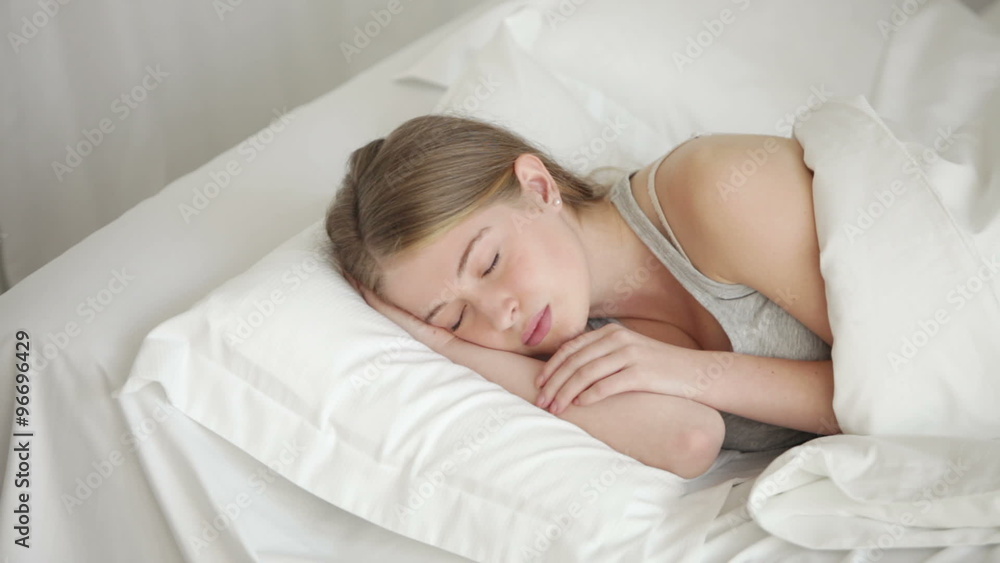 Charming young woman sleeping in bed moving and smiling in her sleep Charming young woman sleeping in bed moving and smiling in her sleep