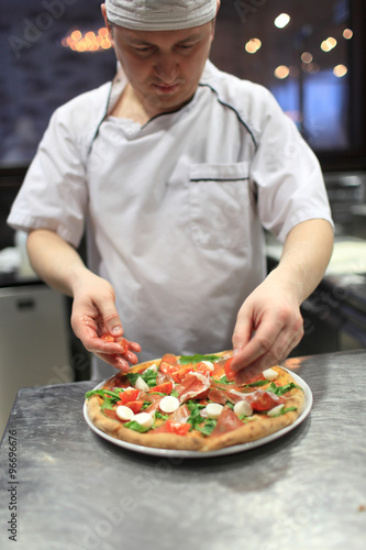 chef baker in white uniform making pizza at kitchen.Focus on the pizza
