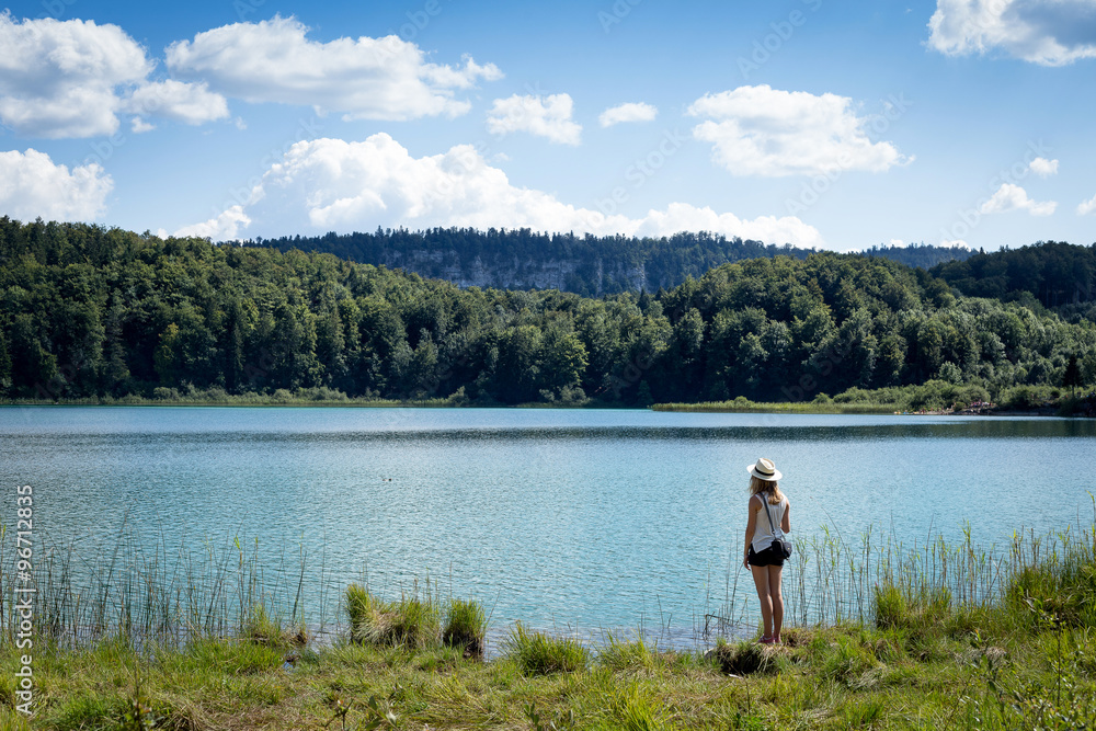 jeune fille avec un chapeau de dos au bord d'un lac en été