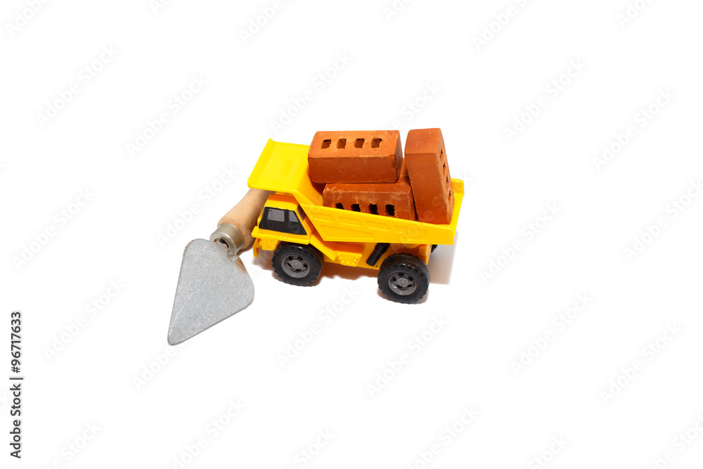 truck with bricks at a construction site. toy car with a body full of toy bricks. trowel tool blocks the path of the truck. Isolated on white background truck with bricks at a construction site. toy car with a body full of toy bricks. trowel tool blocks the path of the truck. Isolated on white background