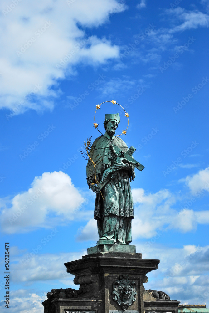 statue of John of Nepomuk in Prague on the Charles Bridge on the background of blue sky with clouds. Czech Catholic saint, priest, martyr