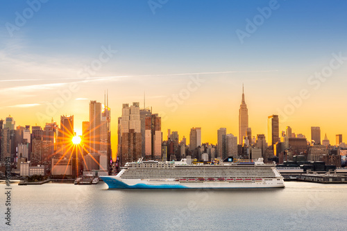 New York City skyline at sunrise  as viewed from Weehawken  along the 42nd street canyon. A large cruise ship sails Hudson river  while sun beams burst between the skyscrapers.