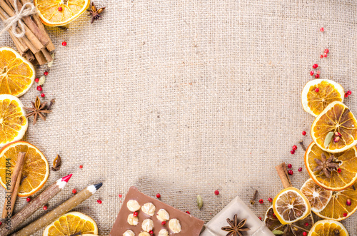 Dried oranges, cinnamon, cloves, cardamom, handmade milk chocolate with nuts, wooden pencil, list of paper on sackcloth, canvas. Christmas, New Year and winter. Free space for your text. photo