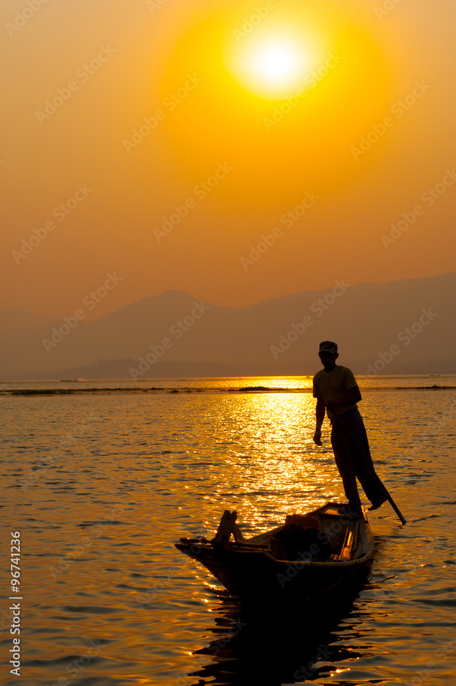 Fototapeta premium INLE LAKE VILLAGE MYANMAR : Silhouette People rows the wooden boat by his leg in Inle Lake