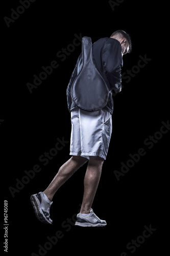 Young athlete walking in white shorts carrying racket cover isolated