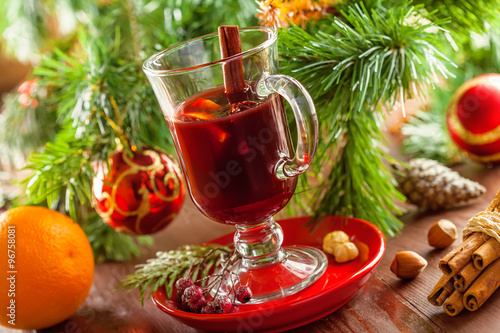 Holiday winter hot drink. Mulled wine with fruits and spices by Christmas tree with decorations.