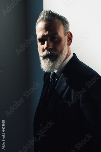 Portrait of bearded man wearing trendy suit and stands against the wall
